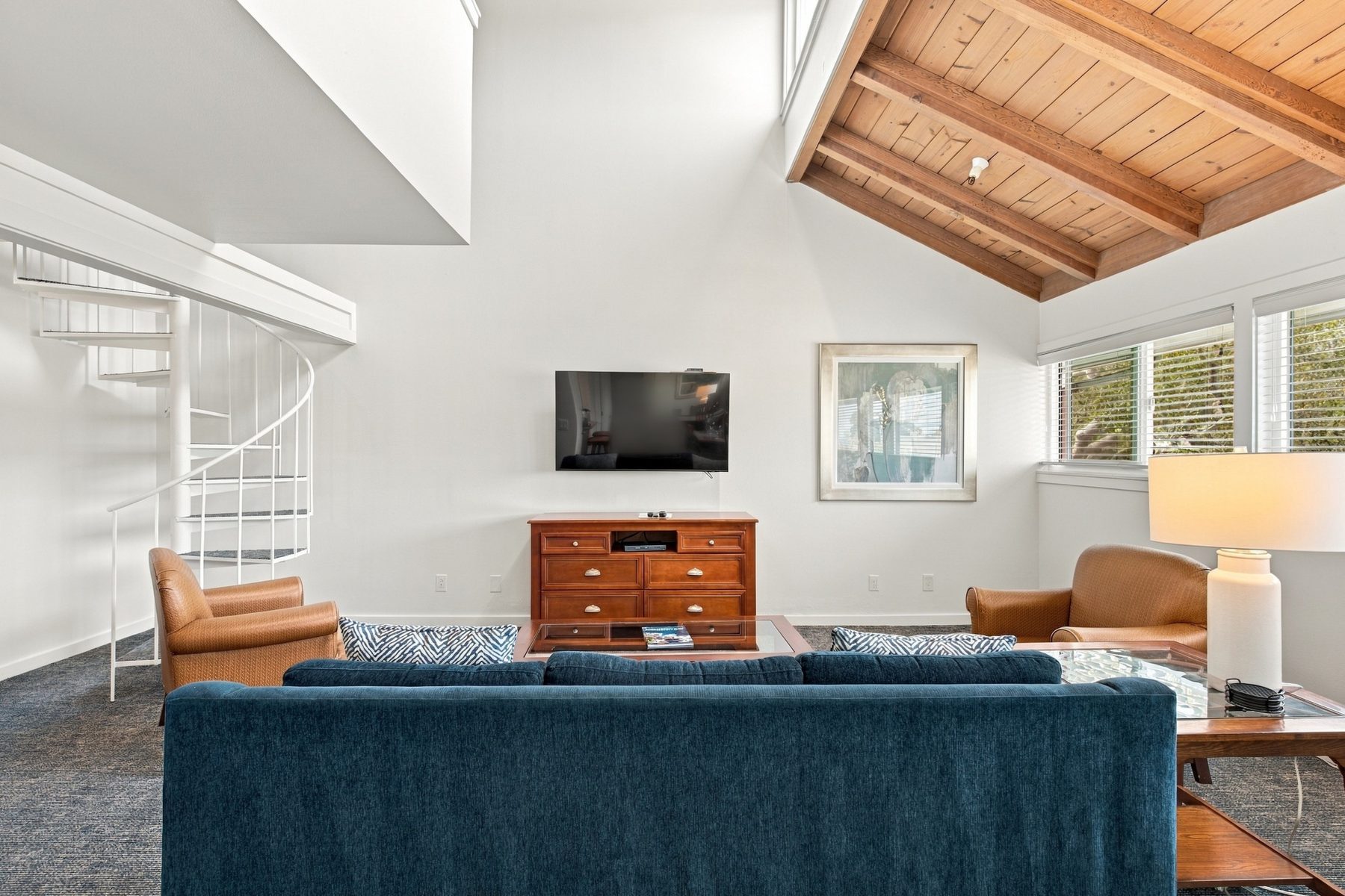 Pacific Grove Plaza suite living room with a vaulted wood-beam ceiling, blue sofa, and spiral stair to the loft